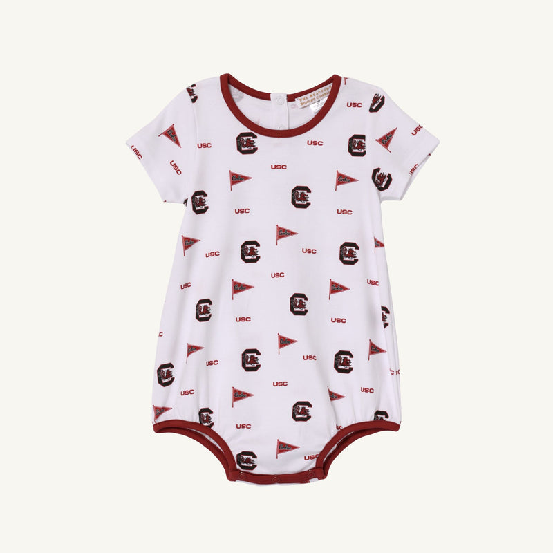 The Beaufort Bonnet Company’s USC Short Sleeve Patton Play Bubble - South Carolina Spirit with South Carolina Burgundy is a white baby romper featuring maroon trim, USC text, pennant flags, and stylized letter C logos in maroon. Crafted from soft Pima cotton, this short sleeve bubble includes snaps at the bottom for easy diaper changes—perfect for showing your South Carolina spirit.