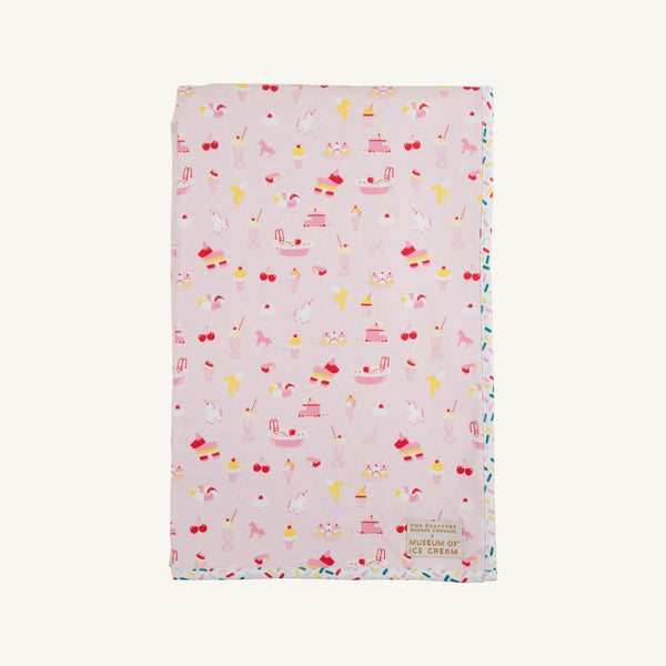 Introducing the Silent Night Throw - Ice Cream Daydream (Strawberry Pink) by The Beaufort Bonnet Company: a soft, light pink blanket adorned with whimsical ice cream-inspired illustrations—cones, sundaes, cherries, and unicorns—finished with a petite Museum of Ice Cream patch in the bottom right corner. Perfect as a picnic blanket or a cozy accent for your home.