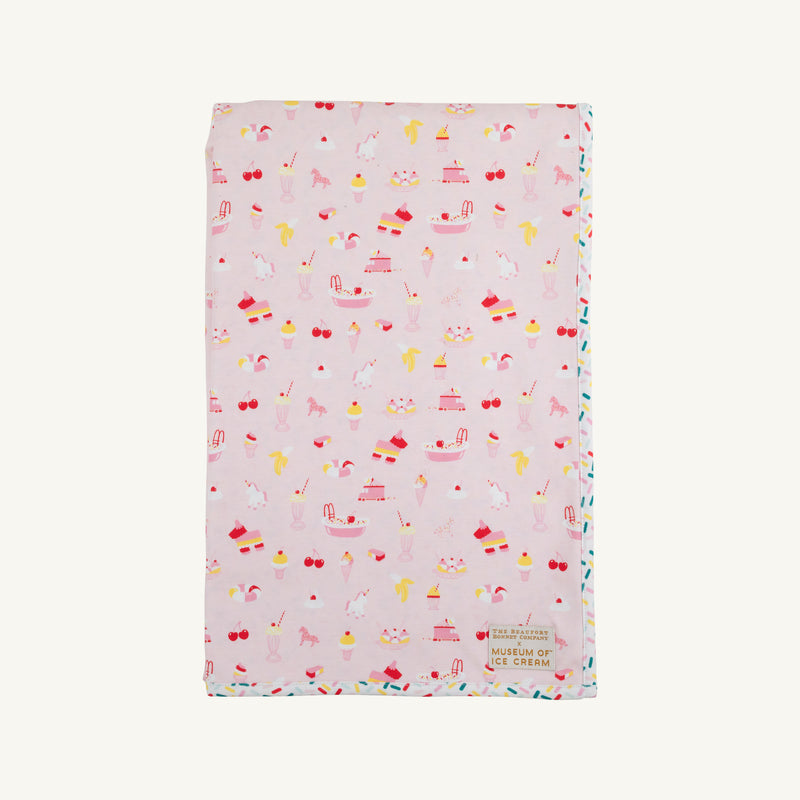 Introducing the Silent Night Throw - Ice Cream Daydream (Strawberry Pink) by The Beaufort Bonnet Company: a soft, light pink blanket adorned with whimsical ice cream-inspired illustrations—cones, sundaes, cherries, and unicorns—finished with a petite Museum of Ice Cream patch in the bottom right corner. Perfect as a picnic blanket or a cozy accent for your home.