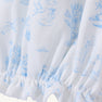 Sir Proper’s Sweet Arrival (Beale Street Blue) Bundle by The Beaufort Bonnet Company features white fabric adorned with light blue illustrations—including a stork carrying a bundle, trees, clouds, houses, and animals. This charming layette gown is gathered with elastic at the bottom edge and comes as part of an adorable everyday set with Bradley Bear, making it a thoughtful baby shower gift.