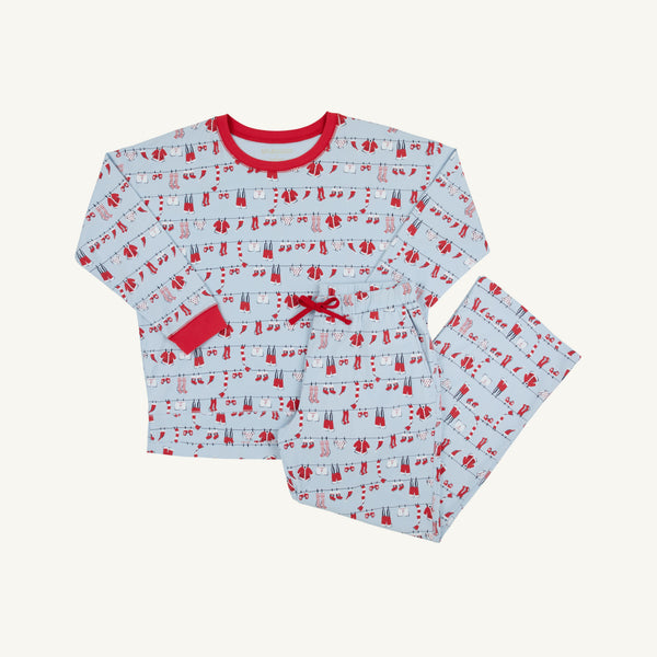 The Snooze Button Set - Santa’s Laundry Line by The Beaufort Bonnet Company is a festive children’s pajama set featuring a white background with red trim and a whimsical print of red and blue winter clothing hanging on clotheslines. This Christmas set includes a cozy long-sleeve top and matching pants, perfect for comfortable holiday lounging.