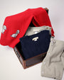 A red Isaac’s Intarsia Sweater - Richmond Red with Grantley Gray and Dogs with a dog pattern, a navy cable-knit, and two gray sweaters, one with button details, displayed in and around a vintage suitcase.