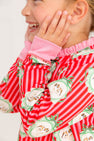 A child wearing a The Beaufort Bonnet Company Cassidy Comfy Crewneck - Distinguished Doggies with Hamptons Hot Pink, featuring a red and pink striped pattern with dogs in circular frames and bright pink ribbed trim at the collar and cuffs.
