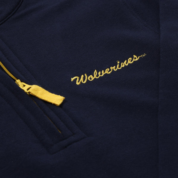 A close-up of The Beaufort Bonnet Company’s Michigan Hayword Half-Zip in Michigan Blue with a Michigan Yellow zipper, featuring “Wolverines” embroidered in yellow script above the pocket.