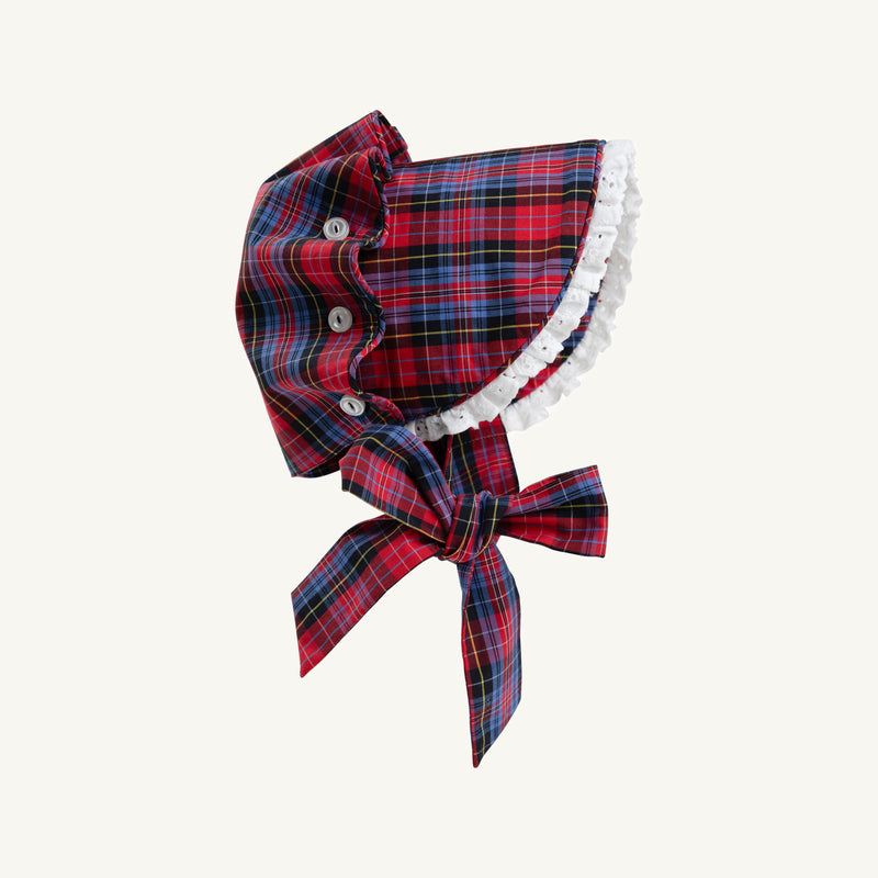 Bellefaire Bonnet - Bucktown Tartan with Worth Avenue White Eyelet by The Beaufort Bonnet Company features a red and blue Bucktown Tartan plaid, finished with delicate Worth Avenue White eyelet ruffle trim and a large coordinating bow at the neck. Displayed against a plain light background, this heirloom-inspired holiday bonnet adds timeless charm to any festive occasion.