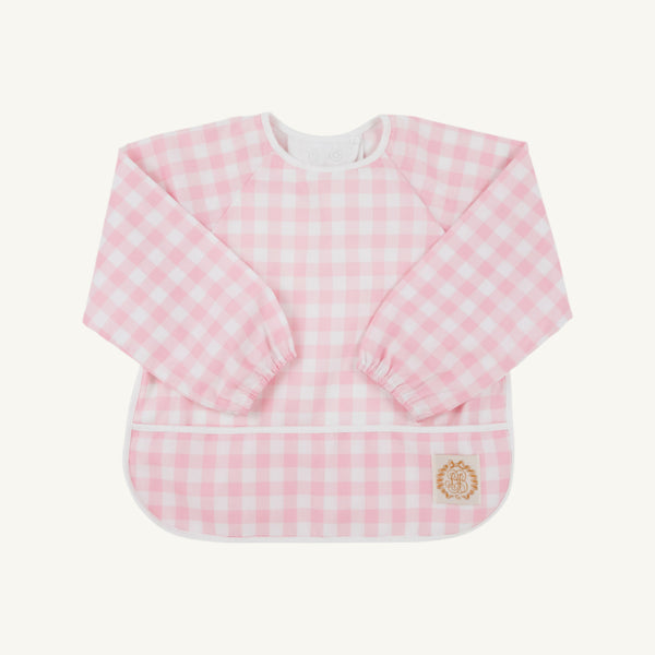 The Beaufort Bonnet Company Biscuit Bib in Palm Beach Pink Gingham with Worth Avenue White trim features long sleeves and a front pocket, shown laid flat against a plain background.