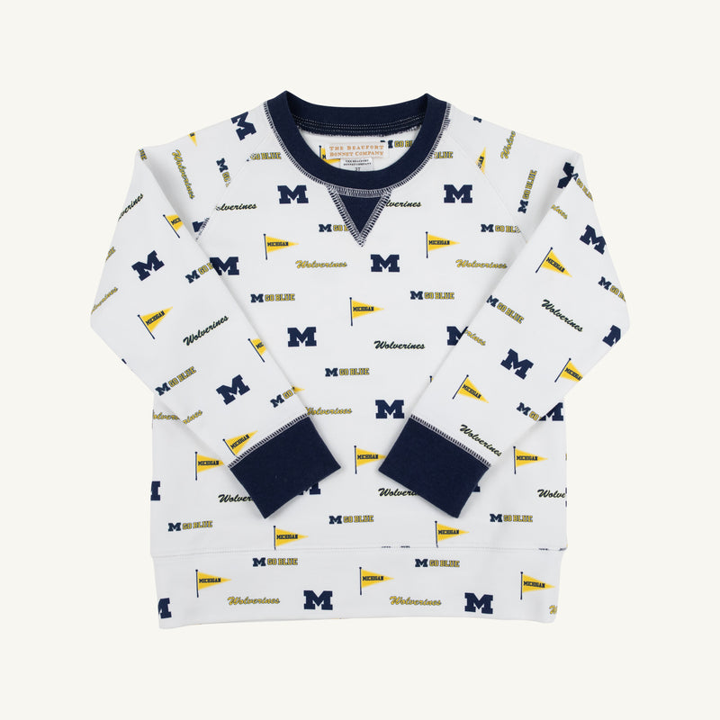 The Beaufort Bonnet Company’s Michigan Cassidy Comfy Crewneck - Bold in Blue with Michigan Blue offers cozy comfort for kids and features navy cuffs and collar, adorned with repeating University of Michigan M logos, pennants, and “Wolverines” text in blue and yellow for spirited school pride.