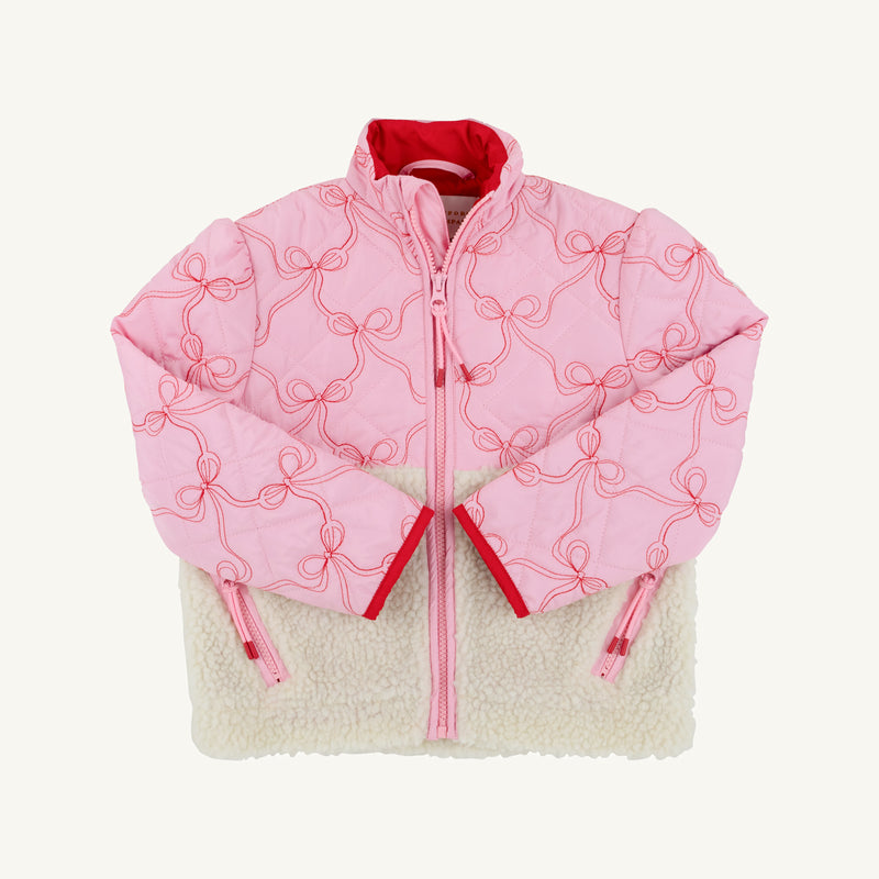 Introducing the Cate Coat - Bluffton Bows with Palmetto Pearl by The Beaufort Bonnet Company: a pink quilted girl’s coat adorned with embroidered bows outlined in red piping, finished with a red zipper and lining. The bottom half features cozy cream-colored sherpa fleece. Stylishly laid flat on a white background, this charming sherpa winter coat is perfect for keeping little ones warm on chilly days.