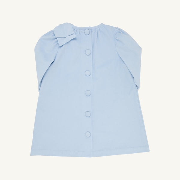 A child’s Dani Dress - Buckhead Blue Corduroy by The Beaufort Bonnet Company is shown from the back. This light blue corduroy dress features a row of buttons down the center and a large bow on the left shoulder, making it perfect for the holidays.