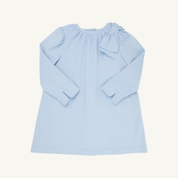 The Dani Dress - Buckhead Blue Corduroy from The Beaufort Bonnet Company is a light blue, long-sleeve holiday dress for children. It features a round neckline, a decorative bow on one shoulder, and simple cuffs. With its loose, comfortable fit, the dress is displayed laid flat on a plain white background.