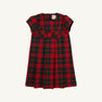 The Darcy Dress - Paces Mill Plaid by The Beaufort Bonnet Company is displayed on a plain white background, showcasing its red and green plaid short sleeves, pleated skirt, and charming bow detailing on the front bodice.