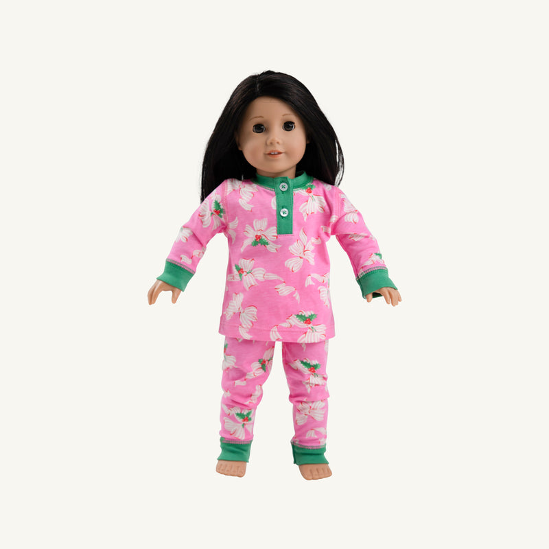A doll with long hair, dressed in Dolly’s Sara Jane’s Sweet Dream Set - Bows of Holly by The Beaufort Bonnet Company—a pink floral pajama set with green cuffs—stands against a plain white background.