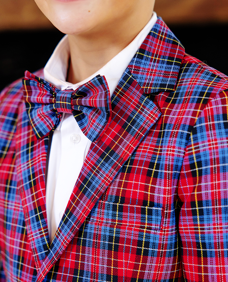 A person wearing a Bucktown Tartan plaid suit jacket paired with The Beaufort Bonnet Company’s Baylor Bowtie in Bucktown Tartan and a white dress shirt, smiling slightly.