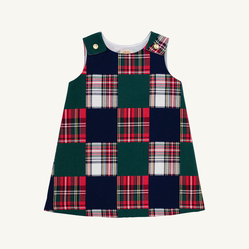 The Juliet Jumper - Mercer Island Madras is a sleeveless toddler dress featuring a checkerboard pattern of solid dark green and red, white, and green plaid squares, with gold-tone button closures on the shoulders.