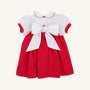 The Mary Dal Dress - Richmond Red & Worth Avenue White with Christmas Tree by The Beaufort Bonnet Company is a festive holiday dress for babies, featuring puffy short sleeves, a Peter Pan collar, charming red buttons, and a large white bow tied at the back—perfect for special holiday occasions or as a Christmas tree dress.