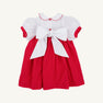 The Mary Dal Dress - Richmond Red & Worth Avenue White with Christmas Tree by The Beaufort Bonnet Company is a festive holiday dress for babies, featuring puffy short sleeves, a Peter Pan collar, charming red buttons, and a large white bow tied at the back—perfect for special holiday occasions or as a Christmas tree dress.