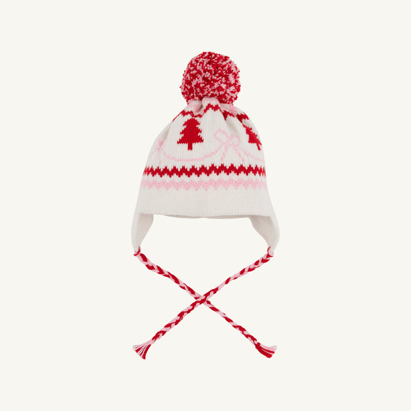 A Parrish Pom Pom Hat in Palmetto Pearl by The Beaufort Bonnet Company, featuring ear flaps, braided tassels, a pom-pom on top, and a festive pattern of bows and Christmas trees.
