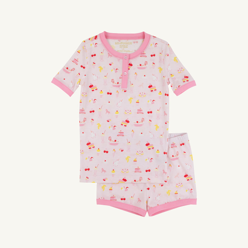 The Beaufort Bonnet Company’s Payton Pajama Shorts Set – Ice Cream Daydream (Strawberry Pink) features a soft cotton jersey children’s pajama set with short sleeves, pink trim, and a delightful dessert-inspired print of cakes, cherries, and ice cream on a white background. This comfy set includes a matching top and shorts for cozy bedtime style.