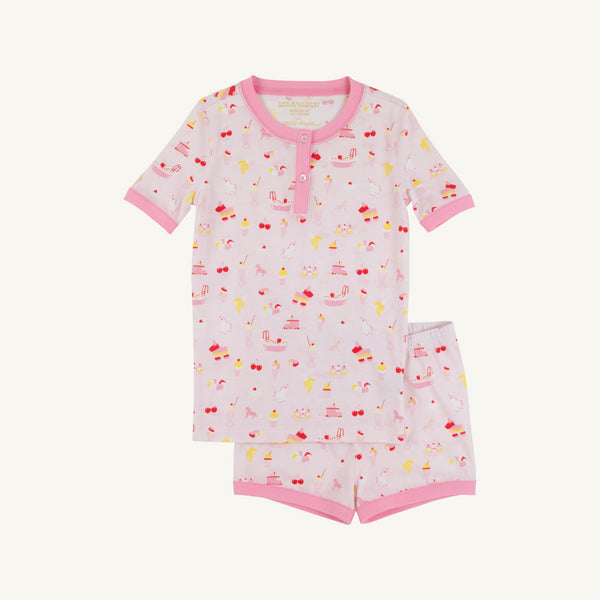 The Beaufort Bonnet Company’s Payton Pajama Shorts Set – Ice Cream Daydream (Strawberry Pink) features a soft cotton jersey children’s pajama set with short sleeves, pink trim, and a delightful dessert-inspired print of cakes, cherries, and ice cream on a white background. This comfy set includes a matching top and shorts for cozy bedtime style.