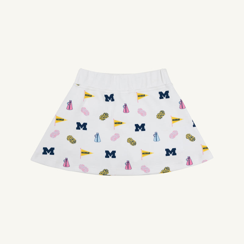 Introducing the Michigan Searcy Skort - Bold in Blue with Worth Avenue White by The Beaufort Bonnet Company, a stylish white Pima cotton skort featuring playful blue M letters, yellow flags, pink pom-poms, and megaphones for a fun school spirit and cheerleading vibe—the perfect new addition to your gameday outfit.