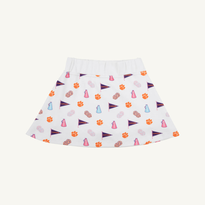 The Beaufort Bonnet Company’s Clemson Searcy Skort - Tiger Triumph with Worth Avenue White features a white, sporty skort with an elastic waistband, playfully patterned with orange paw prints, purple pennants, pink megaphones, and light blue bottles in a repeating design.