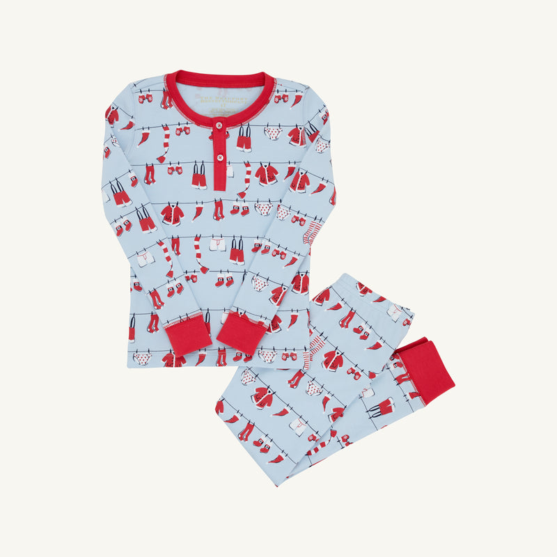 Children’s two-piece Sutton’s Sweet Dream Set - Santa’s Laundry Line with Richmond Red by The Beaufort Bonnet Company, featuring light blue pajamas with vibrant red trim and a charming print of Santa’s laundry—mittens, socks, sweaters, and scarves—hanging on clotheslines. This cozy set includes a long-sleeve top and matching pants, making it perfect for family matching pajamas during the holiday season.